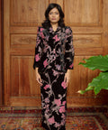 Woman wearing a floral dress standing in front of a wooden paneled wall.