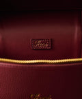 Close-up of a burgundy handbag with gold zipper and visible brand logo.