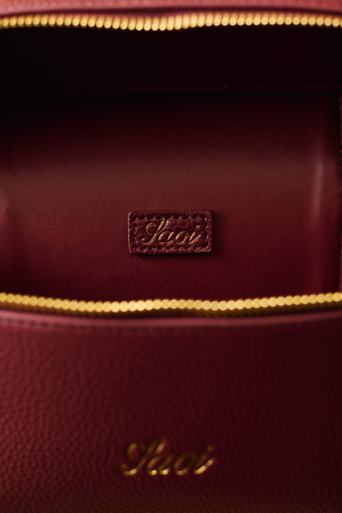 Close-up of a burgundy handbag with gold zipper and visible brand logo.