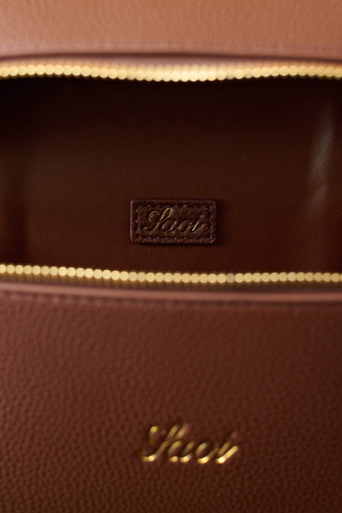 Close-up of a brown leather bag with gold stitching and 'Saoi' branding.