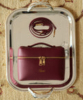 Maroon handbag with gold accents and a strap for crossbody style