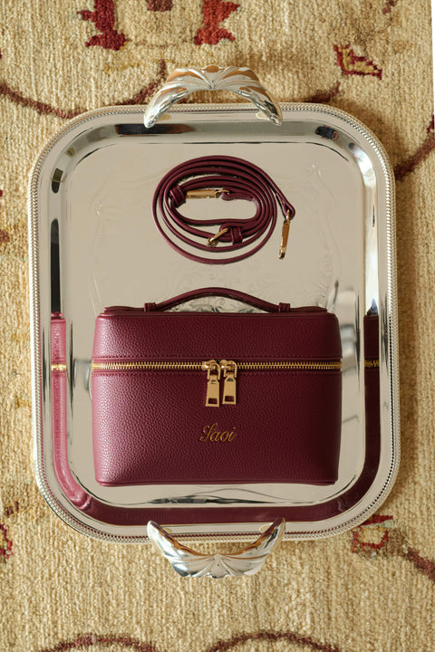 Maroon handbag with gold accents and a strap for crossbody style